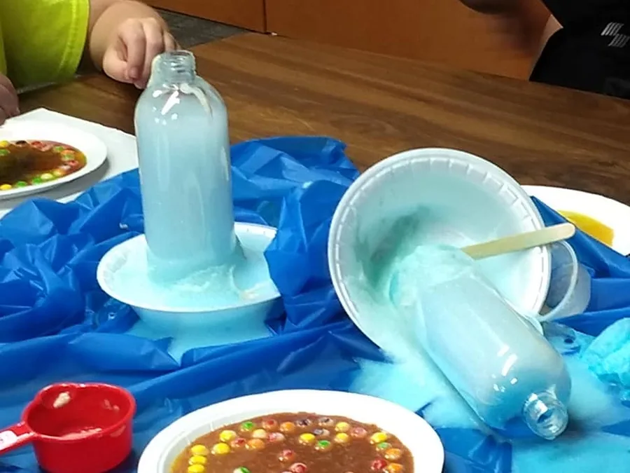 Foam rising out of two bottles onto paper plates, beside a plate of colour-diffusion candies