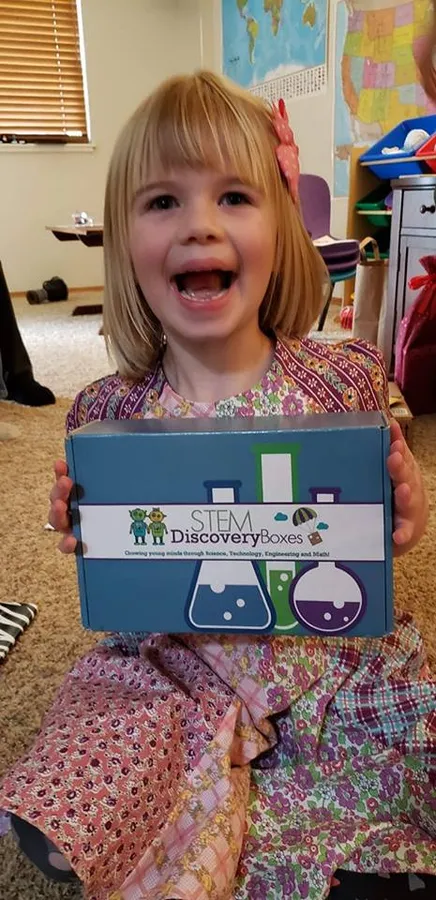 A laughing girl holding a STEM Discovery Box