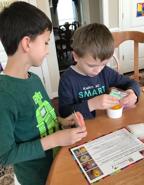 Two boys at a table working on a project with its instruction card