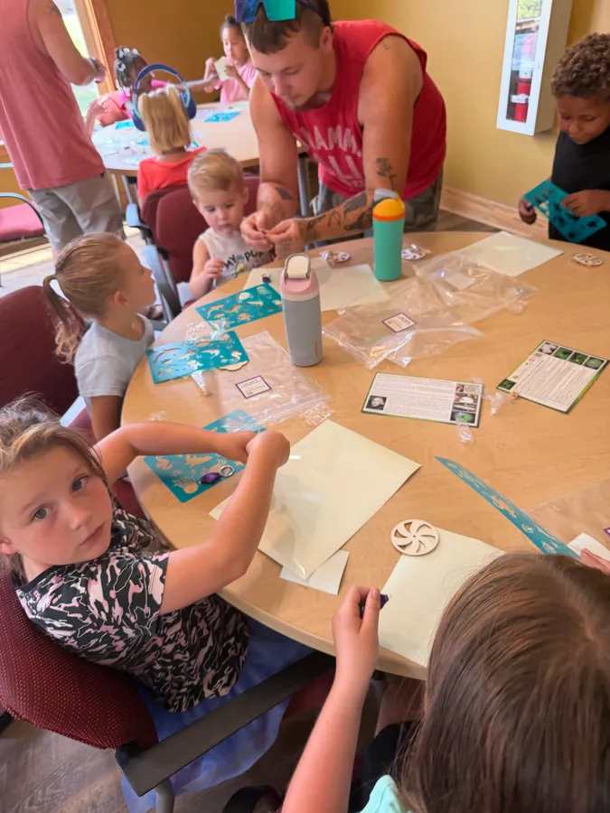 A group of children around a table doing projects with an adult helping