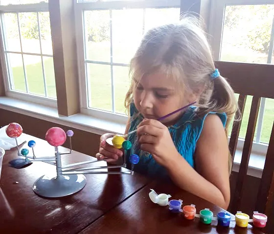 A girl at a table painting the planets of a solar system model