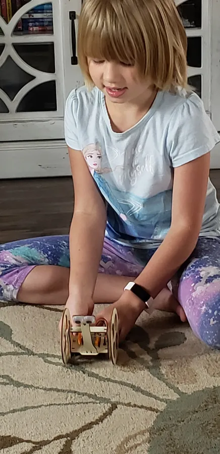 A girl sitting on a rug building a small wooden car