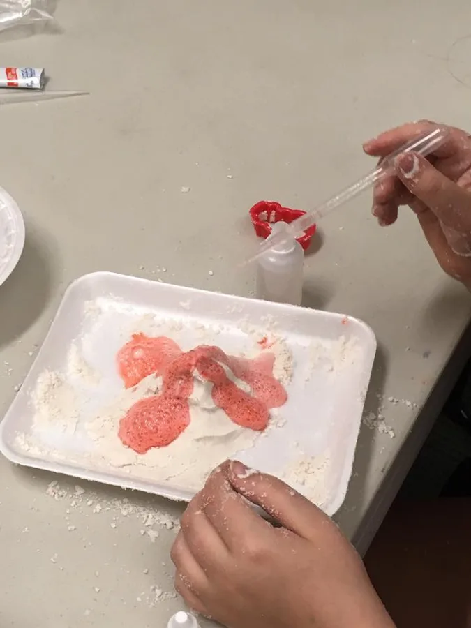 A dropper forming red polymer strands in a tray of white powder