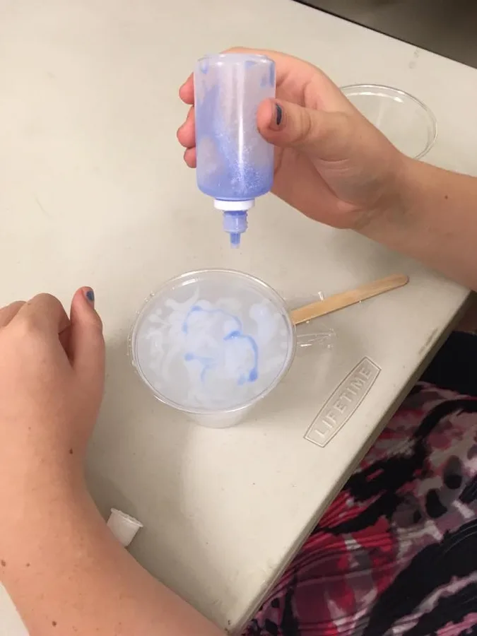 A child squeezing liquid from a bottle into a bowl on a kitchen counter