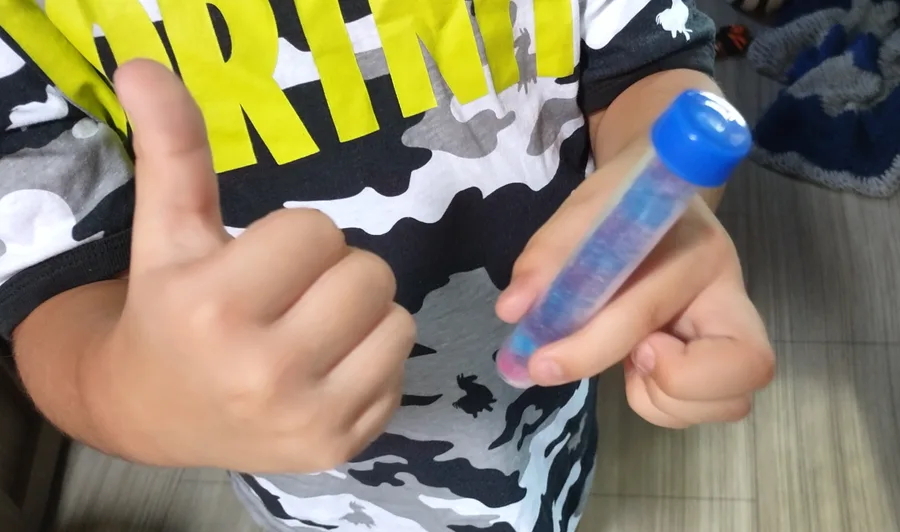 A child holding up a test tube of blue liquid, mid-project