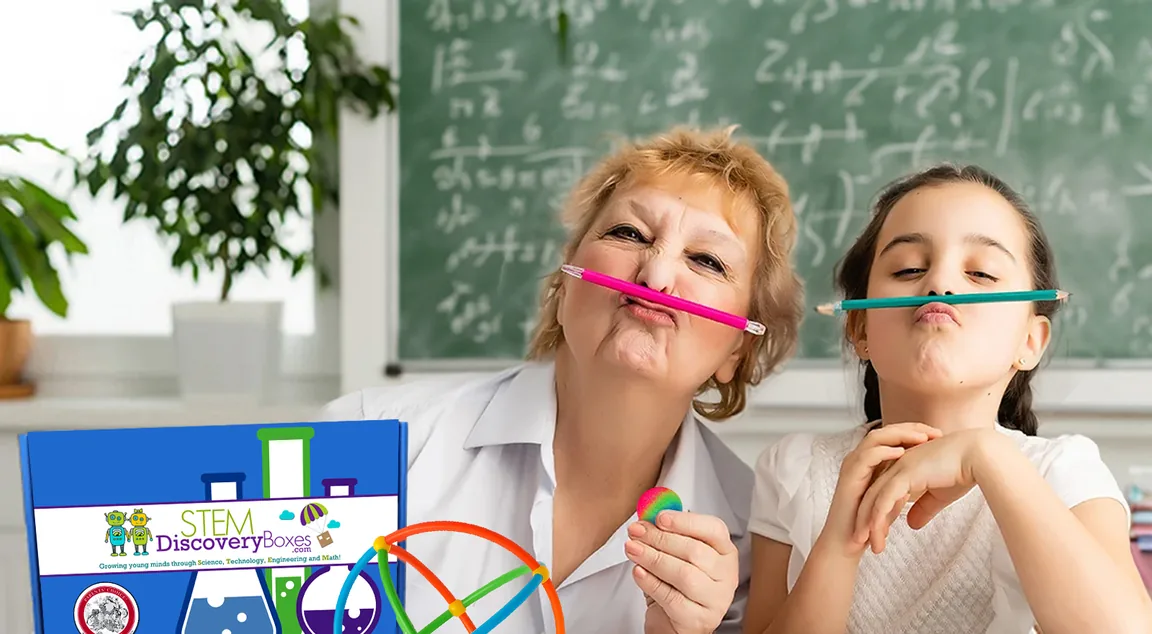 A teacher and a student balancing pencils on their lips at a classroom desk, a STEM Discovery Box beside them