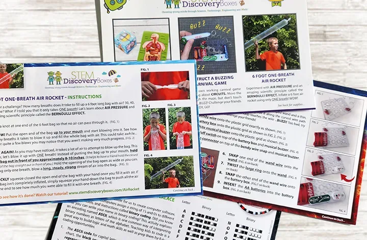 Printed step-by-step instruction and science lesson cards from a STEM Discovery Box, fanned out on a table