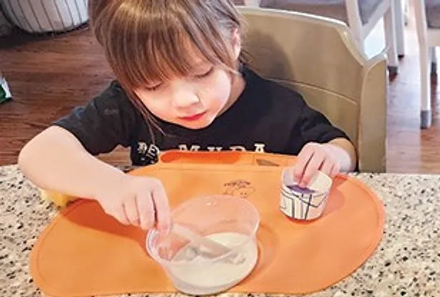 A small child stirring a mixing cup at a kitchen counter