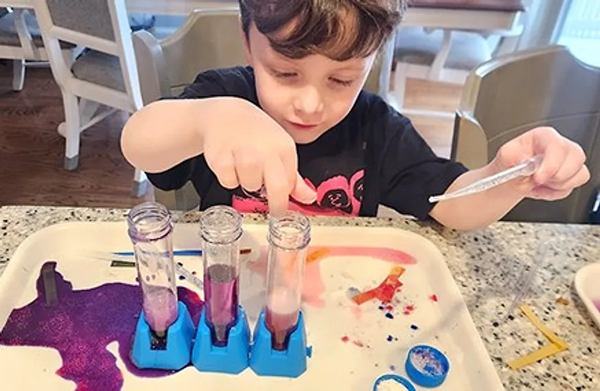 A boy pointing at a rack of test tubes filled with coloured liquid on a kitchen counter