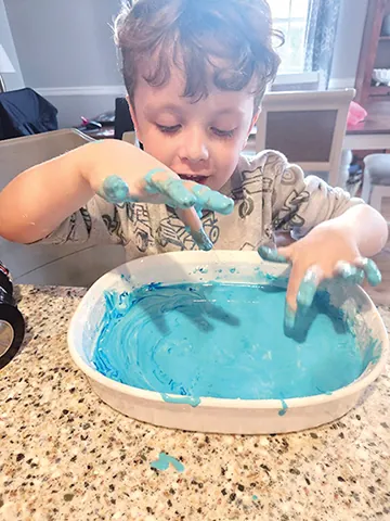 A boy with blue foam up to his wrists in a tray of foaming fountain mix