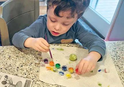 A boy painting with a row of small paint pots on a kitchen counter
