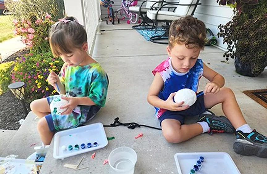 Two young children in tie-dye shirts on a porch with trays of a science project between them