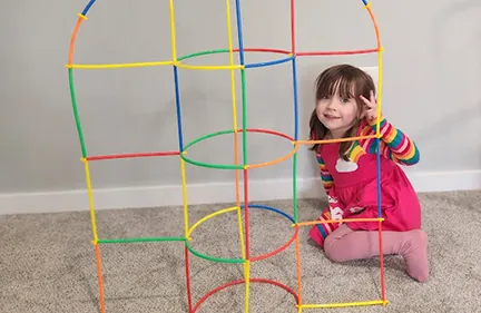 A girl sitting inside the straw structure she engineered, as tall as she is