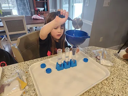 A girl pouring through a funnel into a rack of test tubes on a tray