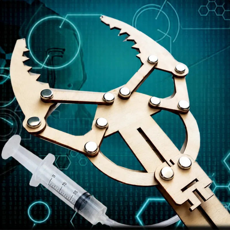 A laser-cut wooden hydraulic claw with metal fasteners, joined by a clear tube to a syringe, on a teal technical background