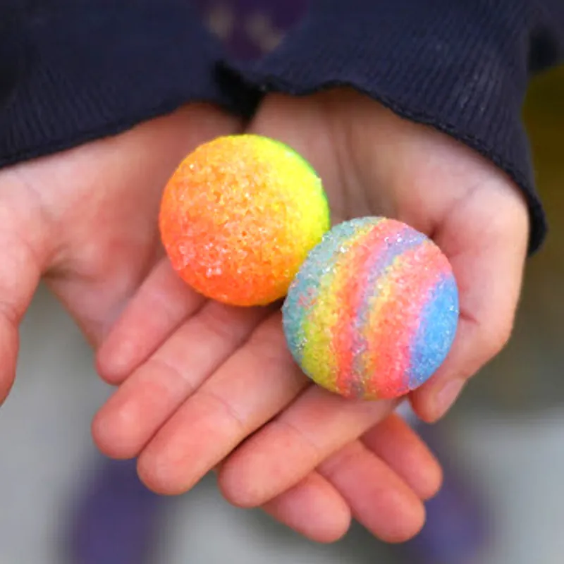 Two hand-made bouncy balls, one orange and one rainbow striped, in a child's cupped hands
