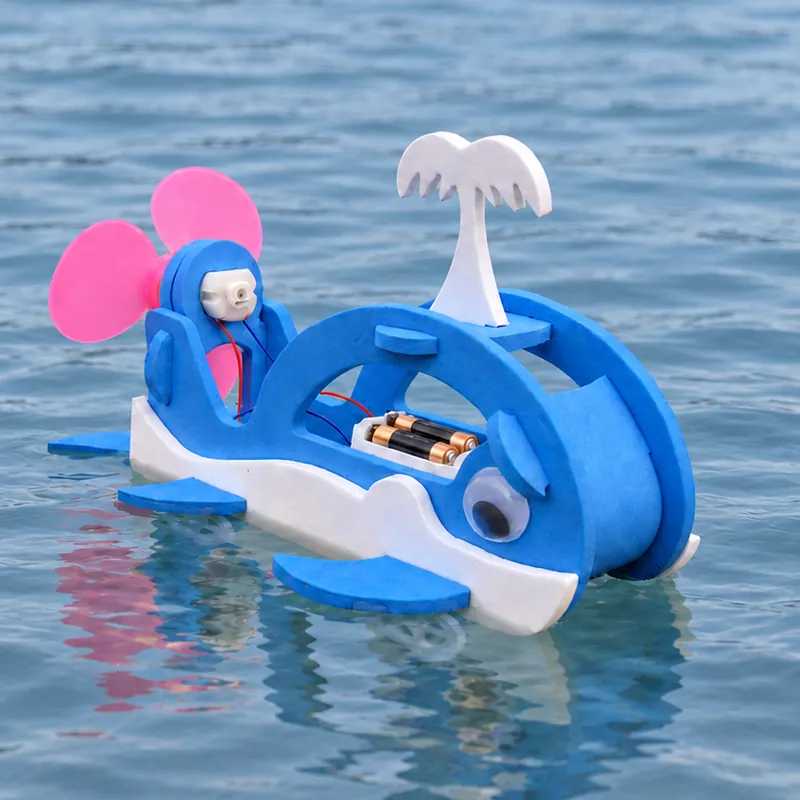 A blue foam whale with a pink propeller and a white spout floating on the water, its battery pack showing